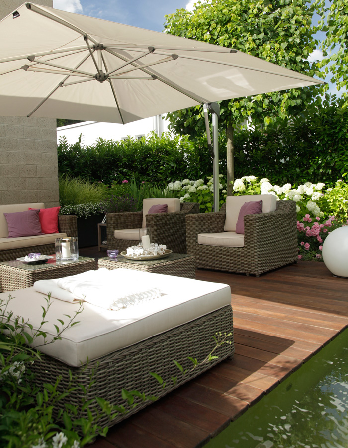 Beige Sonnenschirm über einer modernen Lounge im Garten mit grüner Hecke, Holzterrasse und weißen Blüten – Referenzen von Goroncy.