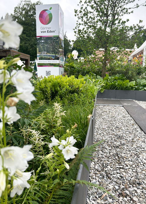Landpartie-IMG_3038 Blühender Garten mit Stauden, Gräsern und Kiesweg neben dem Informationsschild „Gärten von Eden“