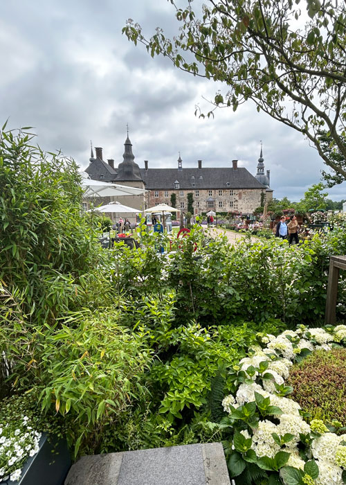 Landpartie-IMG_3058 Historisches Schloss mit Türmen und Innenhof, umgeben von üppigen Gartenpflanzen unter einem bewölkten Himmel